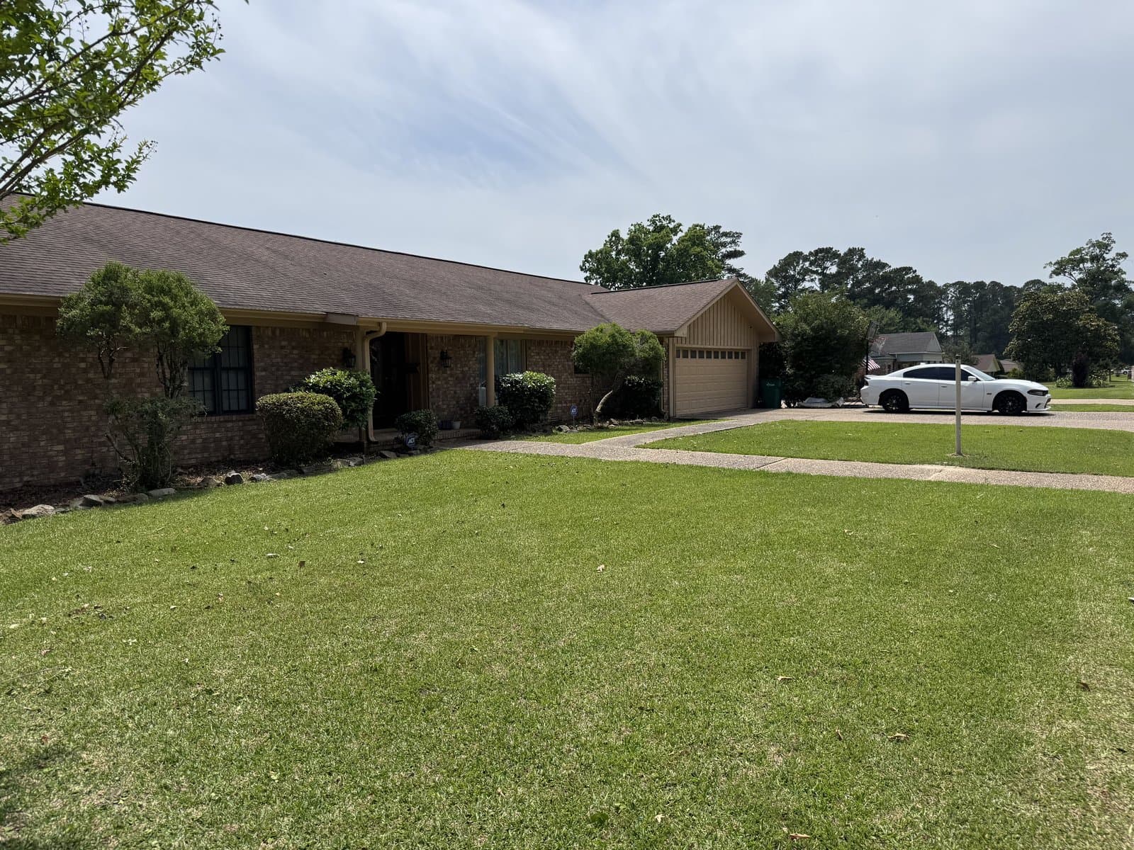 Beautifully manicured brick ranch home with fresh-cut lawn under blue sky